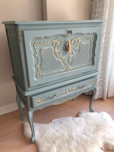 an old dresser painted in blue and gold with white fur on the floor next to it