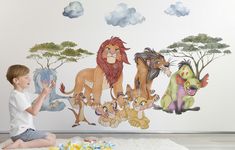 a little boy sitting on the floor in front of a wall with cartoon animals painted on it