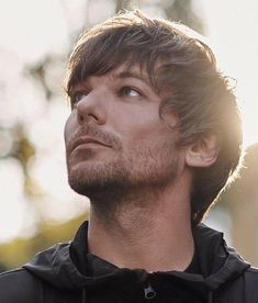 a close up of a person wearing a black hoodie with trees in the background