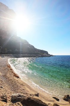 the sun shines brightly on an empty beach with clear blue water and rocky shoreline