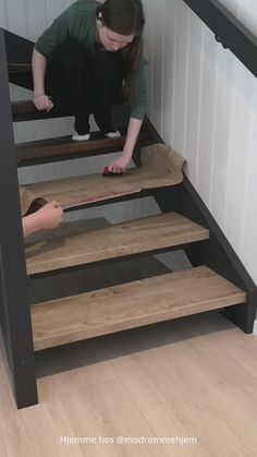 a woman kneeling down on top of a wooden stair case next to another person standing at the bottom