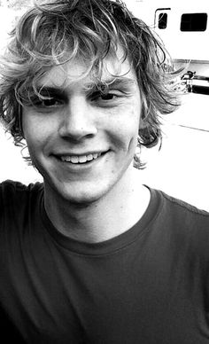 a black and white photo of a young man with curly hair smiling at the camera