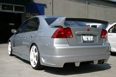 the rear end of a silver car parked in front of a garage with other cars