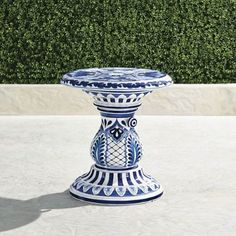 a blue and white vase sitting on top of a cement floor next to a hedge