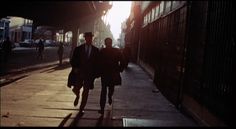 two people walking down the street at sunset or sunrise, with one person wearing a suit and tie