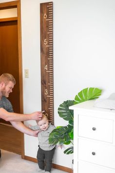 a man holding a small child in his arms near a growth chart on the wall