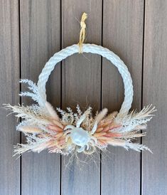 a wreath made out of rope and feathers on top of a wooden wall with a doll hanging from it