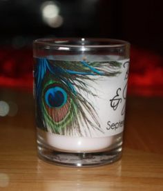 a candle with a peacock feather on it sitting on top of a wooden table next to a red light