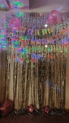 balloons and streamers are hanging from the ceiling in front of a curtain with words written on it