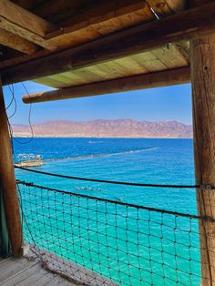 the view from inside a wooden structure looking out at water and mountains in the distance