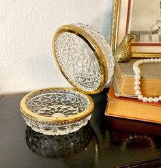 an open glass box sitting on top of a table next to a book and necklace