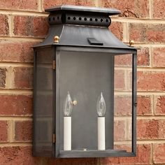 two lit candles are placed on the side of a brick wall mounted light fixture in front of a brick building