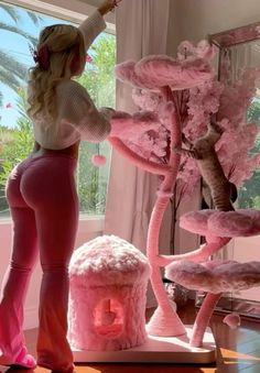 a woman standing in front of a window next to a pink tree and stuffed animals