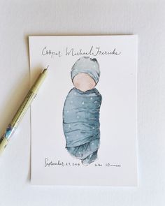 a card with a drawing of a baby wrapped in a blue blanket next to a pen