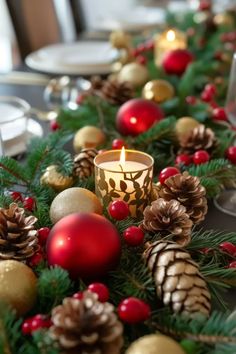 a christmas table setting with pine cones, candles and red balls on the centerpiece