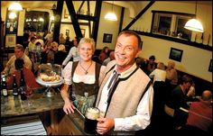 a man and woman standing next to each other at a bar with people in the background