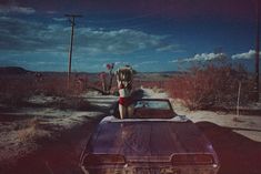 a car parked on the side of a dirt road next to a woman in a bathing suit