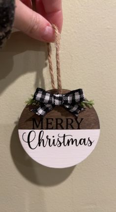 a hand holding a merry christmas ornament hanging on a wall