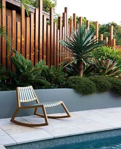 a wooden chair sitting next to a swimming pool in front of a fenced area