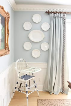 a white chair sitting in front of a window next to a wall with plates on it