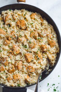 a skillet filled with rice and meat covered in parmesan cheese, garnished with herbs