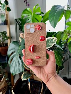 a person holding up a cell phone case with some food on it in front of a potted plant