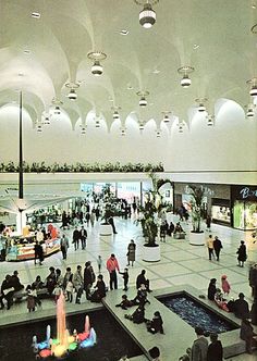 an indoor mall filled with lots of people and water features suspended from the ceiling above