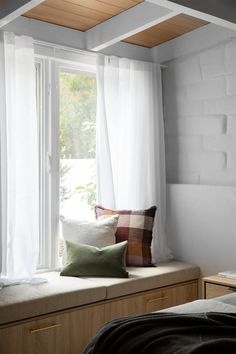 a window seat with pillows on it in front of a bed and windowsills