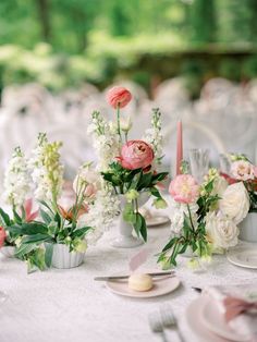 the table is set with pink and white flowers in vases, plates and silverware