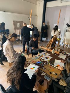 a group of people sitting around a table with art supplies on it and paintings in the background