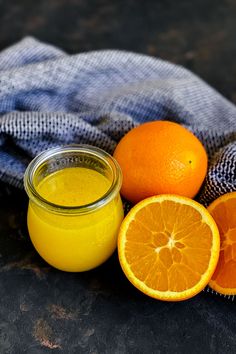 two oranges next to a jar of juice on a cloth with a blue towel in the background