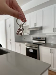 a hand holding a house shaped keychain in front of a kitchen with white cabinets