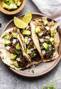 three shredded beef tacos with avocado and cilantro on a plate