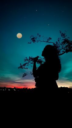 the silhouette of a woman holding a tree branch at night with the moon in the background