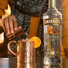 a woman pouring a drink into a copper mug with an orange slice on the rim