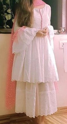 a woman standing in front of a mirror wearing a white dress with pink trims