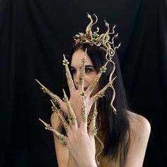 a woman with long black hair wearing a gold crown and holding her hands up to her face