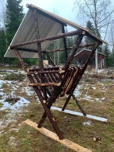 a wooden structure made out of branches in the middle of a field with snow on the ground