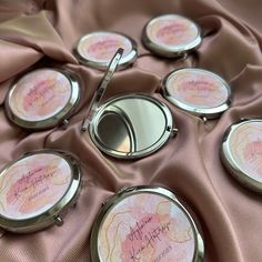 six compact mirrors with writing on them sitting on a pink satin covered tablecloth, next to a pen and mirror