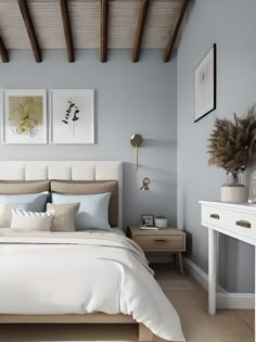 a white bed sitting in a bedroom next to a wooden table and dresser with two pictures on the wall