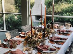 a table set with candles, plates and napkins for thanksgiving dinner in front of a large window