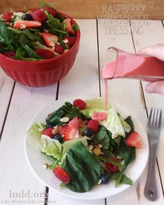 a person pouring dressing onto a salad with strawberries and blueberries on the side