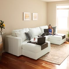 a woman sitting on top of a white couch in front of a window with a laptop