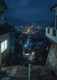 a person riding a bike down a dark alley way at night with city lights in the background