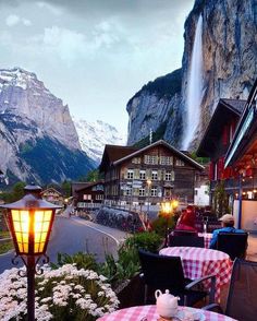 an outdoor restaurant with tables and chairs in front of a mountain waterfall at dusk, surrounded by mountains