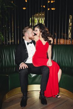 a man in a tuxedo and woman in a red dress sitting on a green couch