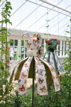 a bell in the middle of some plants and flowers with a bird on it's back