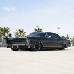 a black car parked in a parking lot next to palm trees and stadium lights on a clear day