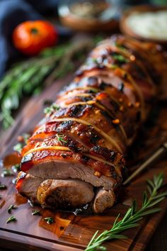 meat wrapped in bacon and garnished with herbs on a cutting board next to tomatoes