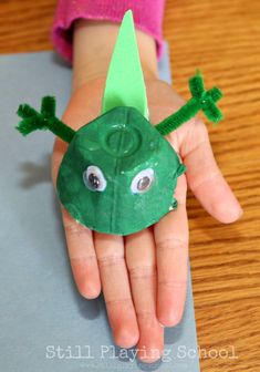 a child's hand holding a paper plate with a green leaf and two googly eyes